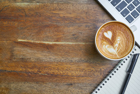 Kaffeetasse mit Cappucchinoschaum auf dem Schreibtisch, mit Notizblock und Computertastatur